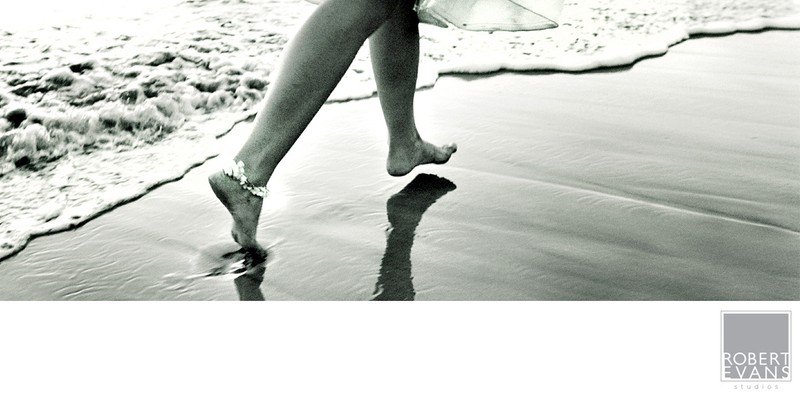 Bare feet walking along the shoreline, reflected in wet sand beside the surf