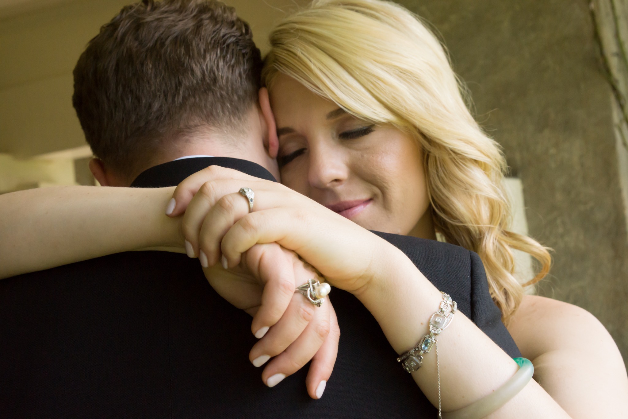 A bride with closed eyes embracing her partner, her hands resting on his shoulder